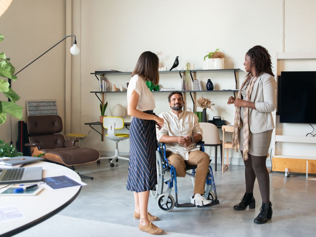 Two individuals conversing with a person in a wheelchair in a modern office setting.